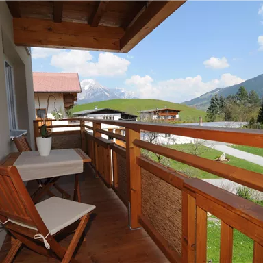 A beautiful balcony with a wooden railing and a view of the mountains. A table and a chair invite you to relax.