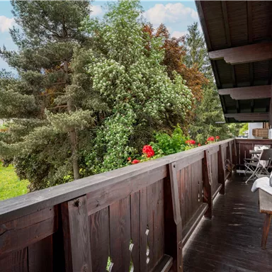 Ein Balkon mit Blick auf üppige grüne Bäume und blühende Blumen. Die Umgebung ist ruhig und lädt zum Entspannen ein.