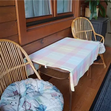 A cozy balcony with two wicker chairs and a colorful table. The table is covered with a blanket and the floor is carpeted.