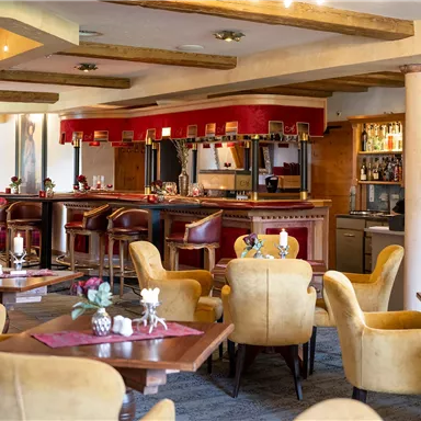 Ein einladendes Restaurant mit komfortablen, gelben Sesseln und Holztischen. Im Hintergrund befindet sich eine Bar mit einer gemütlichen Atmosphäre.
