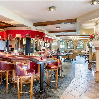 Eine gemütliche Restaurant- und Barumgebung mit roten Barhockern und einer einladenden Atmosphäre. Am Fenster stehen Tische für Gäste und ein Kamin sorgt für zusätzlichen Charme.