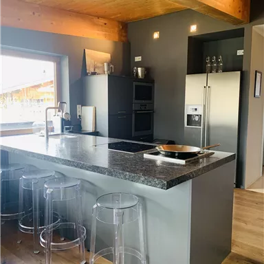Eine moderne Küche mit einer großen Kochinsel und klaren Linien. Die Holzdecken verleihen dem Raum eine warme Atmosphäre.