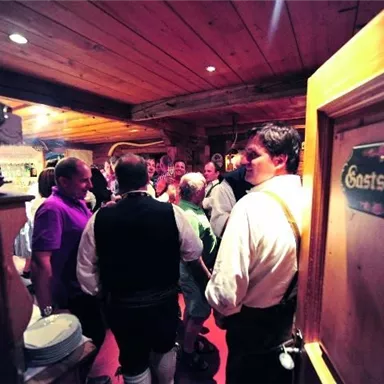 A cozy interior view of a tavern with many guests. The people are standing in a sociable circle and enjoying the atmosphere.