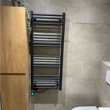 A modern bathroom with a towel warmer on the wall. Next to the towel warmer stands a wooden cabinet.