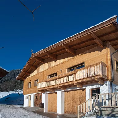 Ein Holzhaus im Schnee mit einem klaren blauen Himmel. Die Architektur ist traditionell und gemütlich.