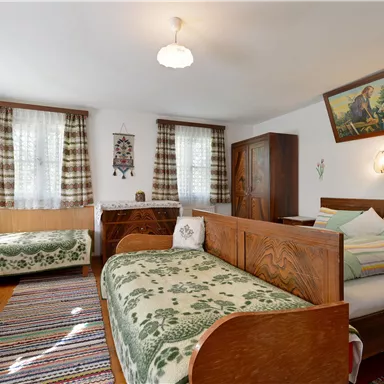 Ein gemütliches Zimmer mit zwei Betten, einem Holztisch und Stühlen. Die Einrichtung ist rustikal mit bunten Teppichen und Vorhängen.