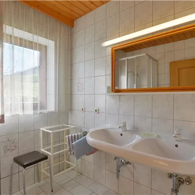 Ein helles Badezimmer mit zwei Waschbecken und einem großen Spiegel. Die Wände sind gefliest und ein Fenster sorgt für natürliches Licht.