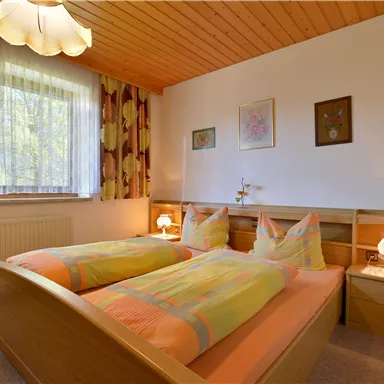 Ein gemütliches Schlafzimmer mit zwei Einzelbetten und bunten Bettdecken. Große Fenster sorgen für viel Tageslicht und eine freundliche Atmosphäre.