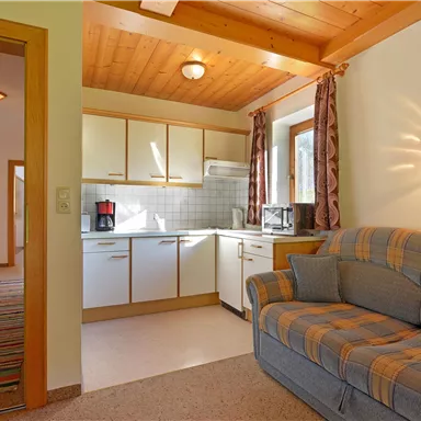 Eine gemütliche Küchenecke mit modernen Küchenschränken und einem Sofa. Die warmen Farben und das Holzdecken-Design schaffen eine einladende Atmosphäre.