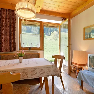 Ein gemütlicher Raum mit einem Tisch und Stühlen. Es gibt ein Fenster mit Blick auf die Landschaft und eine Fernsehecke.