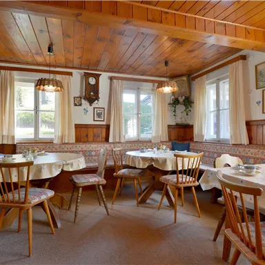 Ein gemütliches Restaurant mit Holzvertäfelung und Tischen, die zum Sitzen einladen. Fenster sorgen für Tageslicht und eine warme Atmosphäre.