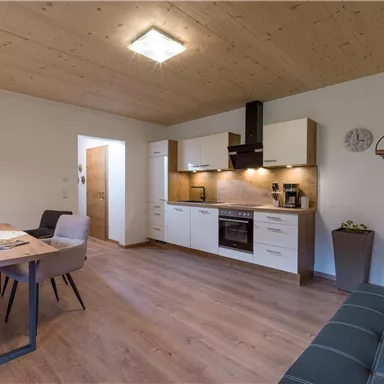 Modern apartment with an open kitchen and a dining area. The space is bright and inviting with wood details and a cozy sofa.