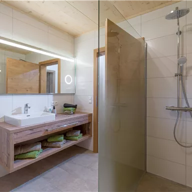 A modern bathroom with a walk-in shower and an elegant wooden vanity. Bright tiles and natural materials create an inviting atmosphere.