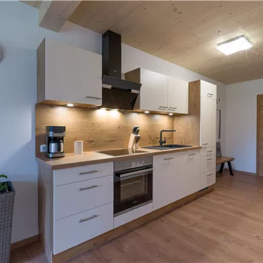 A modern kitchen with wooden shelves and bright cabinets. It is well-equipped and has a warm, inviting look.