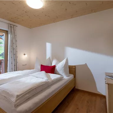 A cozy bedroom with a double bed and white bedspreads. The room has large windows that lead to a balcony with a view of the countryside.