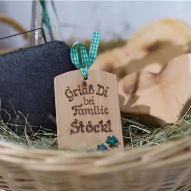 A basket with a wooden sign that says "Greetings from the Stöckl family." Next to it are a stone and some wooden shapes.