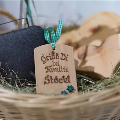 A decorative basket with a wooden sign that says "Grüß Di bei Familie Stöckl." The basket also contains a stone and two wooden hearts.