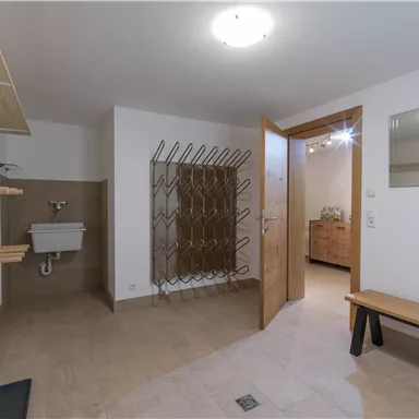 A modern entrance area with bright walls and a wooden shelf. On the right side, there is a wooden bench and an open door to another room.