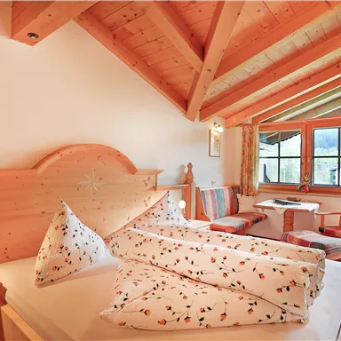 A cozy bedroom with wood decor and large windows. The room is bright and welcoming, with a small table and chairs.