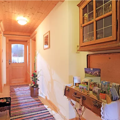 An inviting hallway with a wooden ceiling and a colorful carpet. A dresser with postcards and a plant gives the space a cozy atmosphere.
