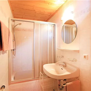 A modern bathroom with a shower cabin and a sink. The walls are brightly tiled and there are towels in soft colors.