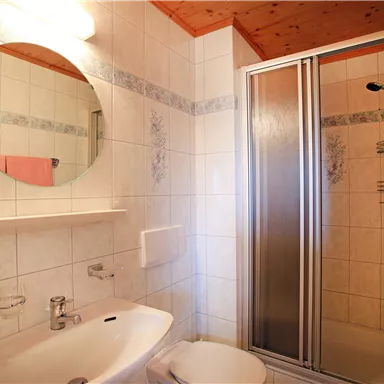 A modern bathroom with a shower enclosure and sink. Bright tiles and wooden cladding create a friendly atmosphere.