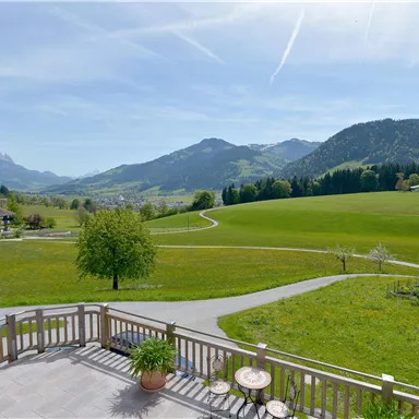 A picturesque landscape with green meadows and gently rolling hills. In the background, there are mountains and a clear, blue sky.
