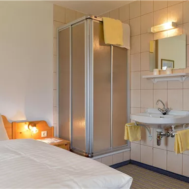 A simple room with a bed, a bathroom with a shower cubicle, and a sink. Bright walls and friendly colors create an inviting atmosphere.