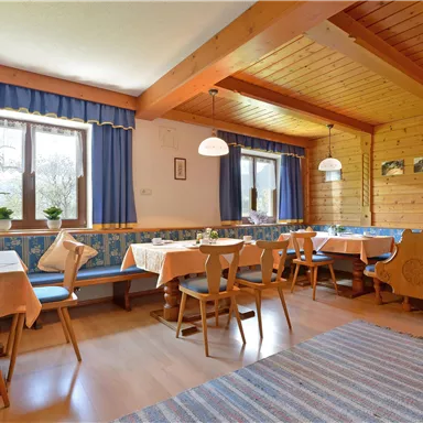 A cozy restaurant with wooden walls and blue curtains. There are tables with tablecloths and "plants" on each table.