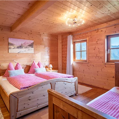 Ein gemütliches Schlafzimmer mit Holzverkleidung und zwei Betten. Die Breite mit karierten Kissen und sanftem Licht sorgt für eine entspannte Atmosphäre.