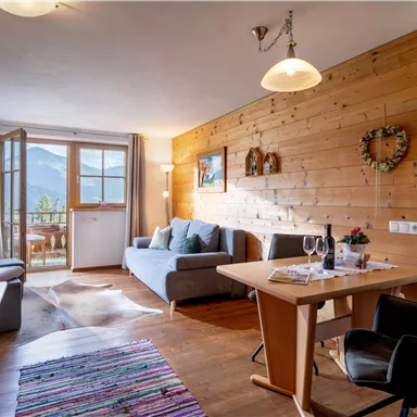 Ein gemütliches Wohnzimmer mit Holzverkleidung und großen Fenstern. Es gibt eine Sitzecke mit einem Sofa und einem Tisch, ideal für Entspannung und Mahlzeiten.