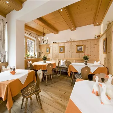 Ein gemütliches Restaurant mit Holzvertäfelung und Tischen in orangefarbenen Tischdecken. Es gibt dekorative Elemente wie Gänsefiguren und Blumenarrangements.