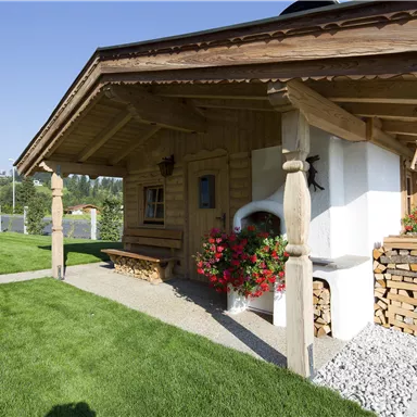 A charming wooden house with a well-maintained garden and flowers. The clear sky and the surrounding nature create an inviting atmosphere.