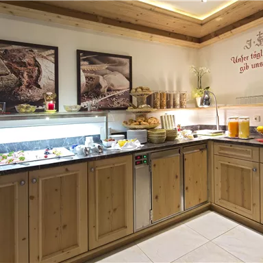 An inviting breakfast buffet with various dishes, fruits, and beverages. The wooden paneling and decorative pictures create a cozy atmosphere.