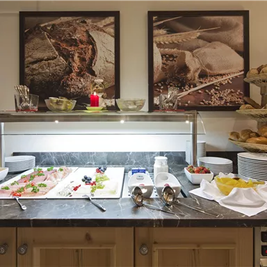 A buffet with a selection of fresh snacks and rolls. In the background, pictures of food are hanging on the wall.