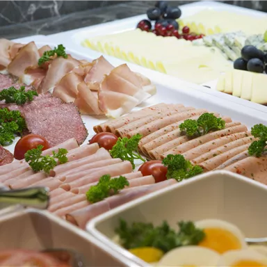 A lavish buffet with various cold cuts, pieces of cheese, and fresh grapes. The food is aesthetically arranged and decorated with fresh parsley.