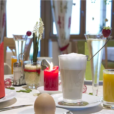 A beautifully set table with breakfast. There is a boiled egg, various drinks, and decorative elements on the table.