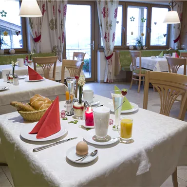 A cozy breakfast room with set tables. The tables are decorated with red and green napkins, alongside fresh bread and drinks.
