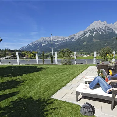 A relaxed terrace with loungers and a view of the mountains. The sky is clear and the landscape is green and inviting.