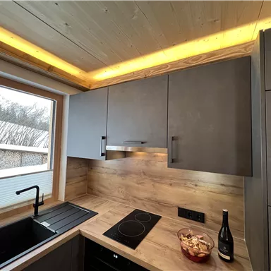 A modern kitchen with wood and gray tones. There is a beautiful view through the window and elegant lighting.