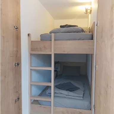 A cozy room with a wooden bunk bed. The bedding is gray and neatly folded.