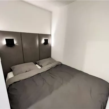 A cozy bedroom with a large bed and modern lighting. The walls are painted in soft, light tones.
