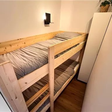 A cozy wooden bunk bed in a modern room. The bedding is simple and the walls are light-colored.