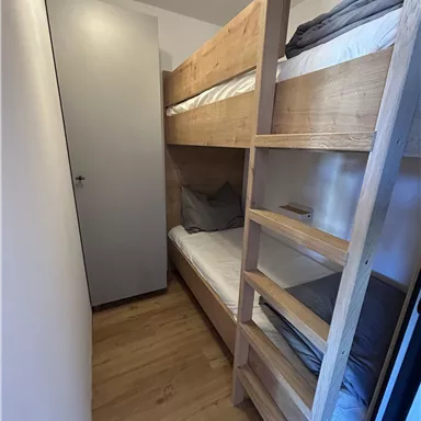 A small room with a wooden bunk bed. The walls are light and the floor is made of wood.