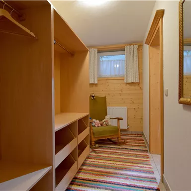 A cozy hallway with a wooden shelf and a comfortable armchair. The floor is covered with a colorful rug, and a mirror hangs on the wall.