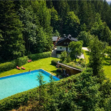 An idyllic house amidst trees with a blue swimming pool. The green space around the house invites you to relax and linger.
