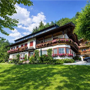 A picturesque house with blooming balconies surrounded by green meadows. The clear sky and trees create an idyllic atmosphere.