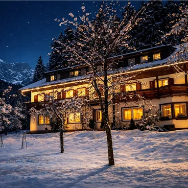 A cozy house in the snow, illuminated by warm light. The night sky is clear and dotted with stars.
