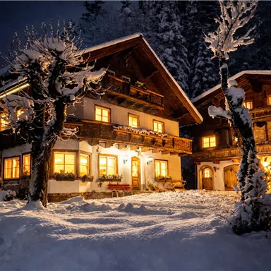 A cozy, illuminated chalet in the snow at night. The surroundings are wintry and idyllic with snow-covered trees.
