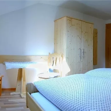 A cozy bedroom with a double bed and a desk. The walls are light, and there are wooden details that create a warm atmosphere.